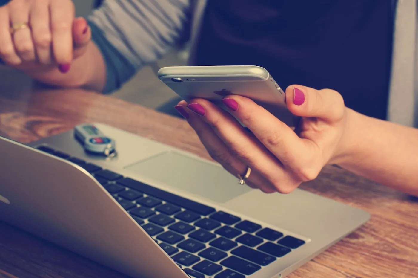 Person reaching out by phone alongside a laptop at a desk